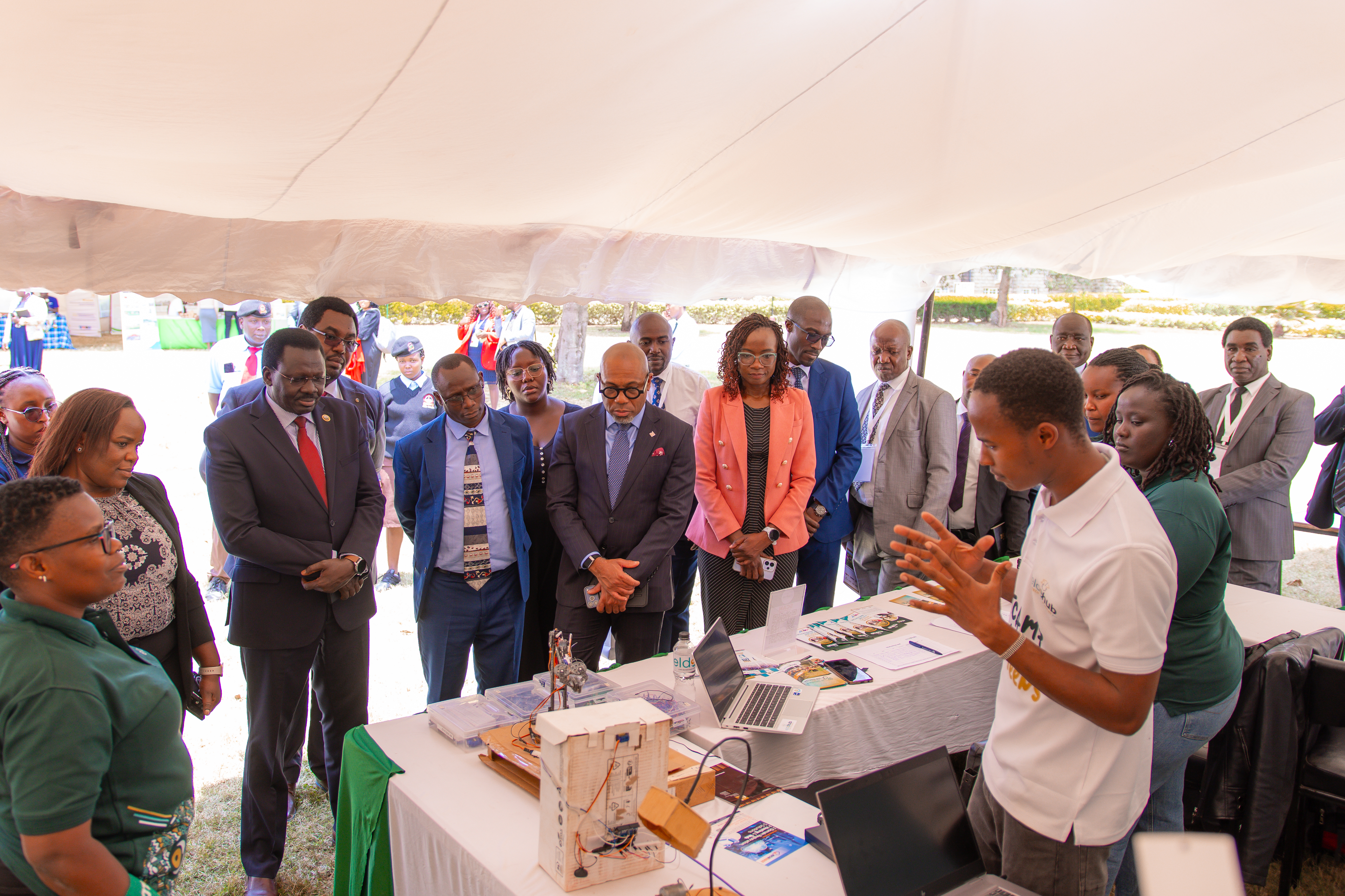 Photo: Prof. Henry Kiplangat (3rd left with a red tie), Kabarak University Vice Chancellor, Stephen Ngeno (4th Left), Deputy Managing Director, Technical Services, and Ralph Opara (5th Left), Access Bank Kenya Country Managing Director, listen to one of the innovators when they toured the exhibition stands during the Innovation Week in Kabarak, Nakuru County.